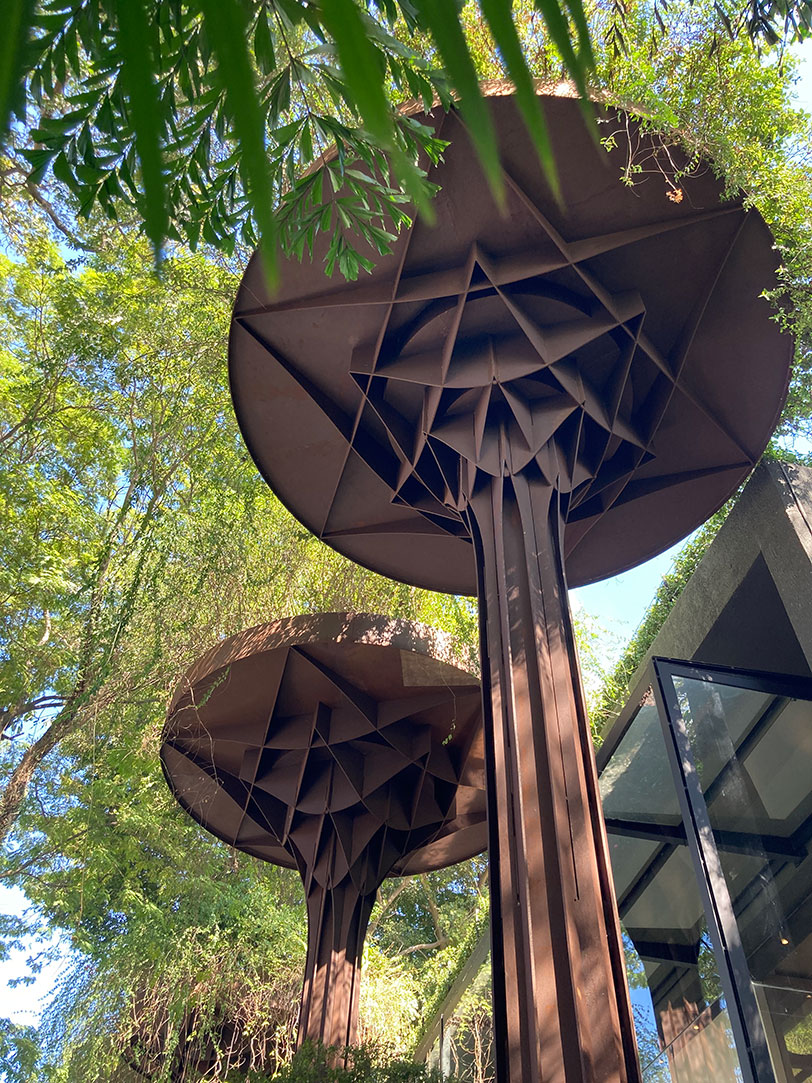 Architectural pedestals create a tree-like canopy of vegetation over the driveway of a commercial building.